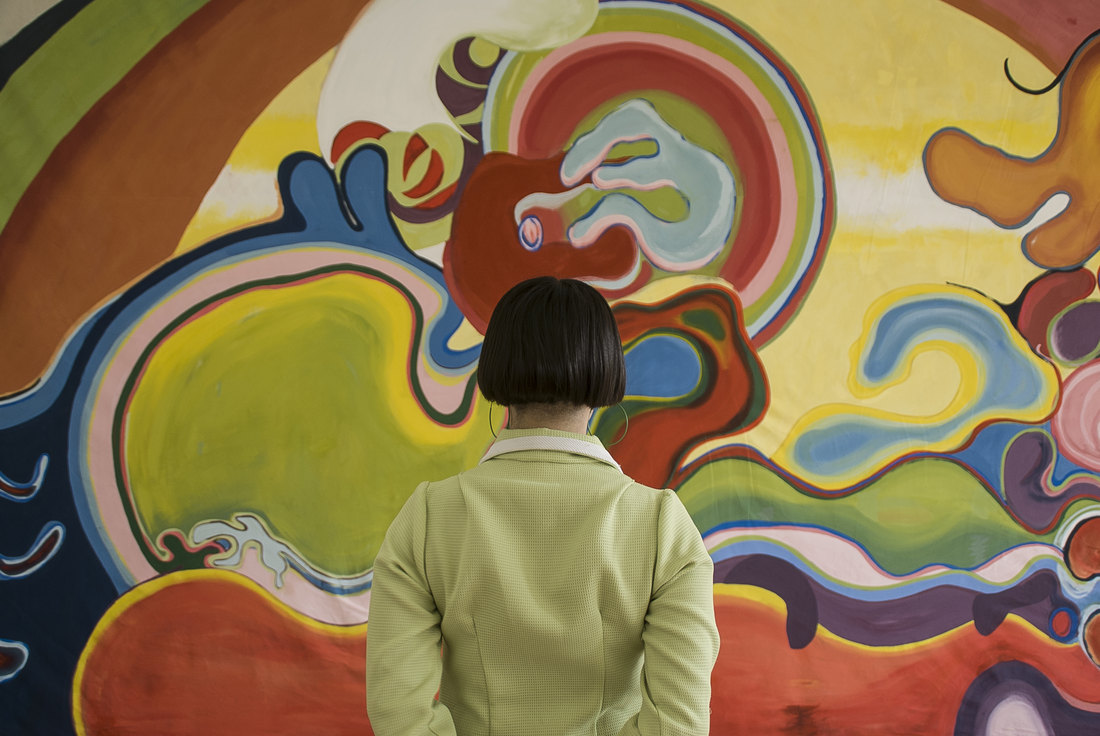 La artista de espaldas frente a una pintura mural de gran escala.