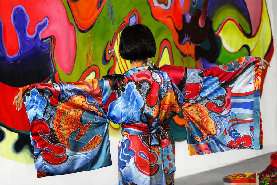 La artista viste un kimono pintado a mano frente a una pintura mural.