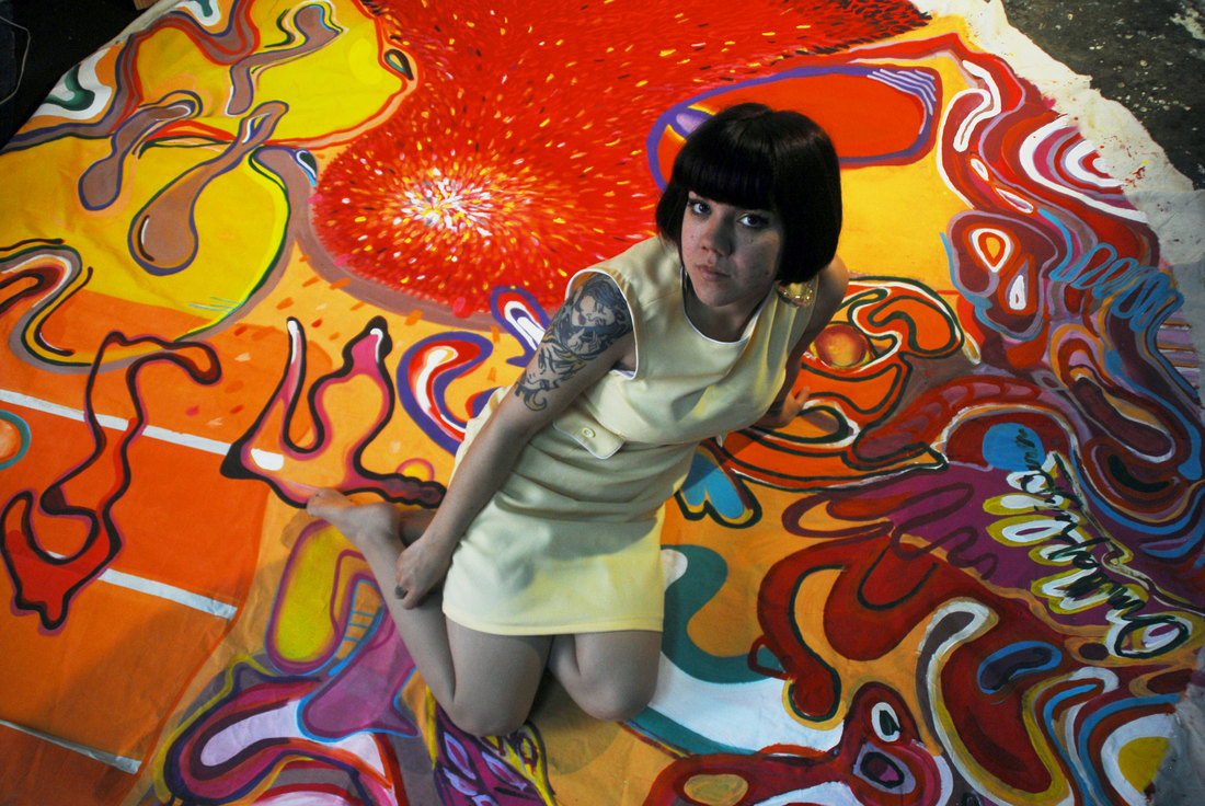 Ornella Ruiz Díaz kneeling on a large-format painting on unstretched canvas, unfolded on her studio floor